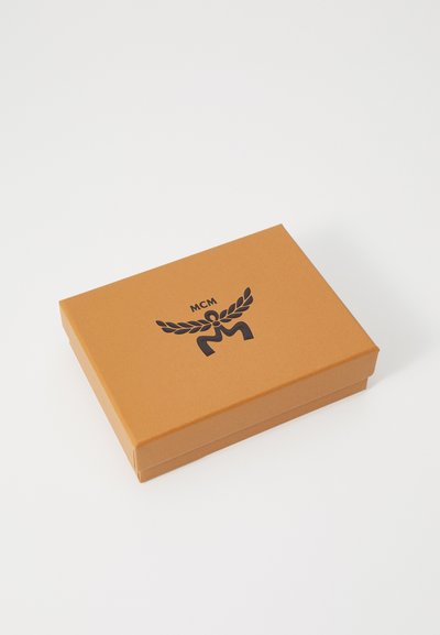 Brun rektangulär låda med en svart logotyp som har en stiliserad figur och vingar på locket. Slät, matt yta. Lockandesign.
