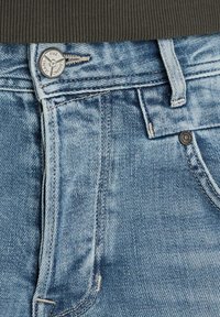 Jeans de mezclilla azul claro con un diseño clásico de cinco bolsillos, con cierre de botón metálico, costuras visibles y una textura ligeramente desgastada.