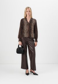 Blusa a stampa leopardata con maniche lunghe, scollo a V e polsini elasticizzati. Pantaloni a gamba larga in ecopelle marrone. Piccola borsa nera in tessuto texture. Scarpe nere appuntite.