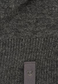 Ciemnoszara, prążkowana dzianina z małym metalowym logo w kształcie podkowy przymocowanym do szarej metki.