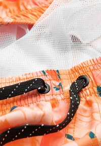 Maillot de bain orange à motif floral avec cordon noir et doublure en mesh blanc visible à travers les plis du tissu.