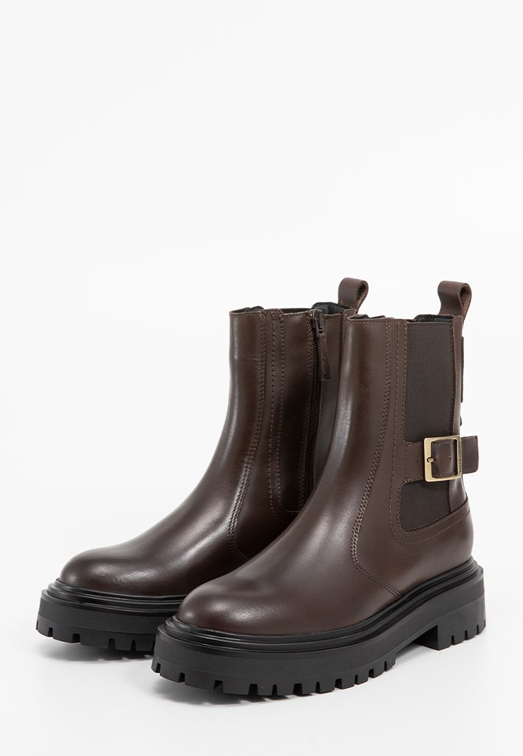 Braune Leder-Ankle-Boots mit strukturierten elastischen Seitenpanels, runder Zehenpartie, massiver schwarzer Sohle und einem goldenen Schnallenakzent.