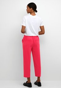 Roze, taps toelopende broek met een verzamelde elastische taille, zijzakken en twee achterzakken, gecombineerd met een eenvoudig wit T-shirt.