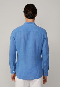 Camicia di lino blu con colletto a rovescio, maniche lunghe con polsini a bottone e orlo dritto, che presenta un tessuto testurizzato e leggermente trasparente.