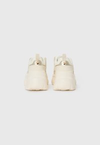 White chunky sneakers with a smooth texture, featuring a cream accent, embossed logo tag, and a round gold detail on the heel.