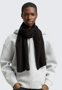 Schwarzer gestrickter Schal, der über einen grauen Reißverschluss-Hoodie drapiert ist. Der Schal hat eine weiche Textur mit einer glatten, gleichmäßigen Oberfläche.