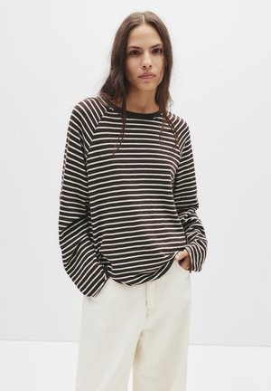 Braun- und weißgestreiftes Langarmshirt mit rundem Ausschnitt und legerem Schnitt. Kombiniert mit hellen Hosen, die eine glatte Textur aufweisen.