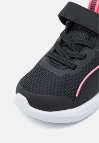 Baskets en maille noire avec des accents roses, dotées d'une sangle Velcro et de lacets. La semelle est blanche et texturée pour une meilleure adhérence.