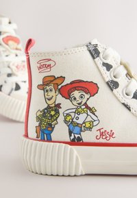 Gros plan d'une basket blanche avec les personnages de dessin animé Woody et Jessie de Toy Story imprimés sur le côté près de la semelle.