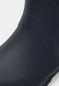 Botte en caoutchouc marine avec une surface lisse, un bout arrondi et un design minimaliste. Pas de matériel ou de motifs visibles. Semelle texturée pour une meilleure adhérence.