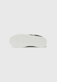 Semelle de sneaker noire présentant un motif en caoutchouc texturé, un contour blanc et un design courbé. Surface plate avec une finition lisse.