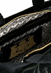 Zwarte fluwelen handtas met gouden beslag, interieur met een contrasterende witte voering met zwart schrift, meerdere compartimenten en ritssluitingen.