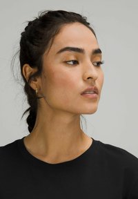 Svart t-shirt med rund hals. Bäraren har långt, mörkt, vågigt hår stylat i en fläta och enkla hoopörhängen i guld.