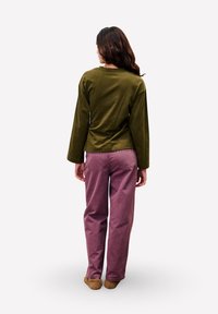 Groene lange mouwen top met een ronde halslijn, gecombineerd met loszittende, roze broeken. Schoeisel zijn bruine, gestructureerde instappers.