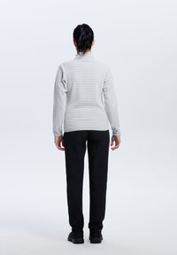 Top gris con patrón de manga larga y cuello alto, combinado con pantalones negros ajustados y zapatos negros, capturado desde la parte trasera.