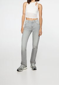 Jeans de color gris claro con un corte recto, diseño de cinco bolsillos y un desgaste sutil, combinados con un top corto de canalé blanco y zapatillas grises.