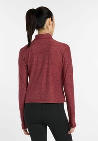 Maroon long-sleeve athletic top with a collar and thumbholes, featuring a textured fabric and a fitted silhouette, paired with black leggings.