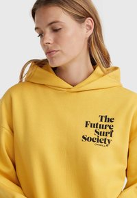 Żółta bluza z kapturem wykonana z miękkiego materiału, z przednim nadrukiem zawierającym tekst "The Future Surf Society" w czerni. W zestawie regulowany kaptur.