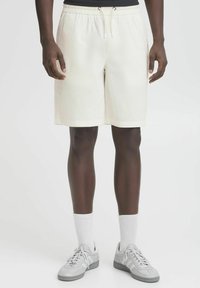 Cremefarvede shorts med elastisk talje, snøre detaljer og lige ben design. Båret med grå sneakers og hvide sokker.