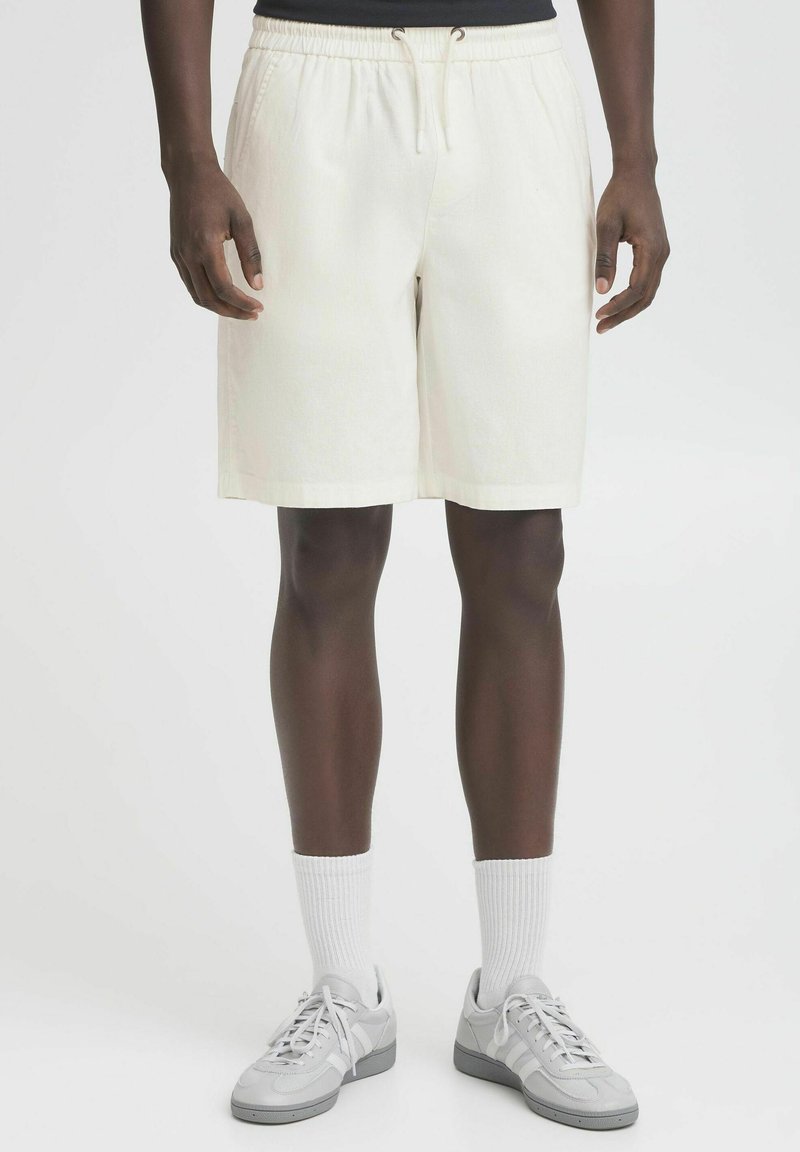 Crème-kleurige shorts met een elastische tailleband, trekkoorddetail en een recht silhouet. Draag ze met grijze sneakers en witte sokken.