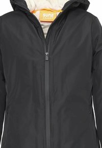 Giacca impermeabile nera con chiusura a zip, interno morbido e cappuccio. Dotata di tasche laterali e di un logo prominente all'altezza del collo.