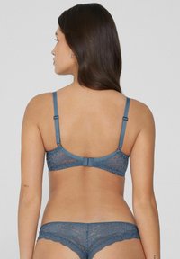 Modrý krajkový podprsenka s nastavitelnými ramínky, zapínáním na háček a květinovým vzorem. Sada doplňují odpovídající krajkové kalhotky s vlnkovanými okraji.
