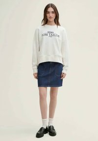 Λευκό φούτερ με γραφικό "TOM TAILOR", συνδυασμένο με μία σκούρα τζιν φούστα, κάλτσες μέχρι το γόνατο και μαύρες λοφάρες. Απλή, casual εμφάνιση.