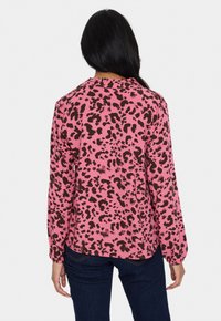Blus med rosa leopardmönster som har långa, samlade ärmar och en rundad nederkant. Tyget har en slät textur och en avslappnad passform.