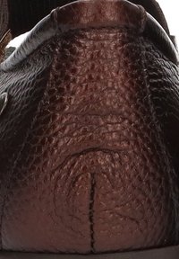 Primer plano de un zapato de cuero marrón, con una superficie texturada, forma redondeada y un sutil detalle de costura en la parte trasera.