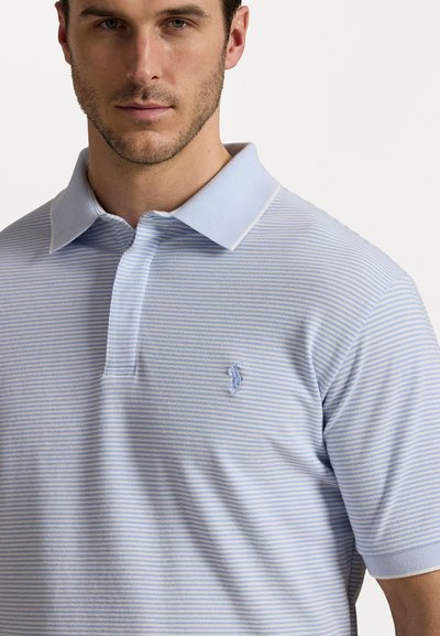 Lyseblå polo skjorte med tynne striper, korte ermer og krage. Har et brodert logo på venstre bryst. Strukturert stoff.