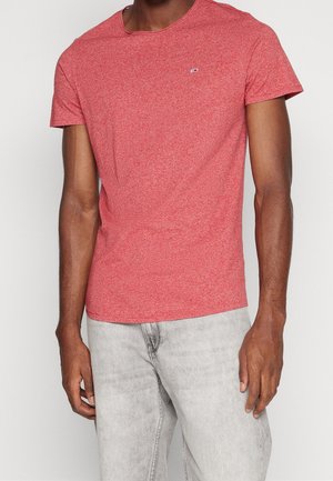 Mand iført en tætsiddende kortærmet T-shirt i lyserød melange med rund hals og lysegrå denimjeans, stående med armene afslappet ned langs siden.