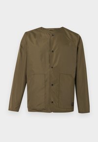 Μπουφάν σε ελαιί πράσινο με μακριά μανίκια, στρογγυλή λαιμόκοψη, κούμπωμα με κουμπιά σούστες και δύο μπροστινές τσέπες σε λευκό φόντο.