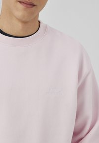 Sweatshirt rose clair en coton doux. Il présente un col rond et un texte brodé "hors série n°1" sur la poitrine. Texture lisse.