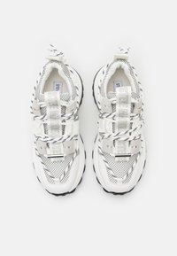Vita idrottsskor med meshtopp, svarta detaljer, tjock gummisula och kontrasterande snören med logodetaljer på remmarna.