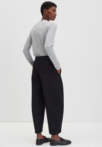 Grijze langetermijn shirt, hoge taille zwarte broek en zwarte schoenen. De broek heeft twee achterzakken; gladde textuur, ontspannen pasvorm.