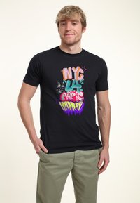 Camiseta de algodón negra con texto estilo graffiti en varios colores que dice "NYC LA PARIS LONDON", con una textura suave y un diseño ajustado.