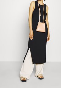 Černé bezramínkové šaty se bočním rozparkem, kombinované s krémovými širokými kalhotami a béžovými platformovými sandály. K nim je nošená malá, strukturovaná světle růžová kabelka.