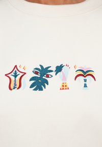 Λευκό φούτερ με πολύχρωμο κέντημα τεσσάρων γραφικών σχεδίων: ένα φυτό, ένα χέρι και διακοσμητικά σχήματα σε μπλε, κόκκινο και ροζ.