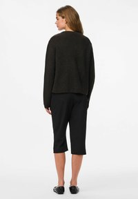 Sweater noir texturé avec une coupe ample, associé à un pantalon noir cropped. La tenue présente un design simple et minimaliste.