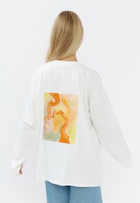 Witte lange mouwen t-shirt met een kleurrijk abstract aquarelontwerp op de achterkant, met oranje, groen en gele tinten. Losse pasvorm.