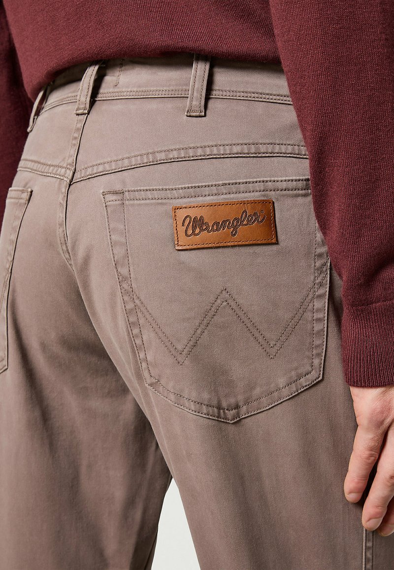 Pantaloni khaki con un'etichetta in pelle Wrangler, caratterizzati da grandi tasche posteriori con un design a cucitura zigzag. Tessuto morbido.