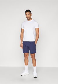 Camiseta blanca de manga corta con un logotipo sutil, combinada con pantalones cortos azul marino y zapatillas deportivas blancas. Tejido de algodón suave y corte relajado.