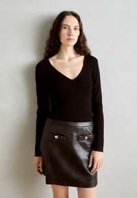 Haut en maille côtelée noire avec un col en V, associé à une mini jupe en cuir noir avec deux poches avant et des accents métalliques.