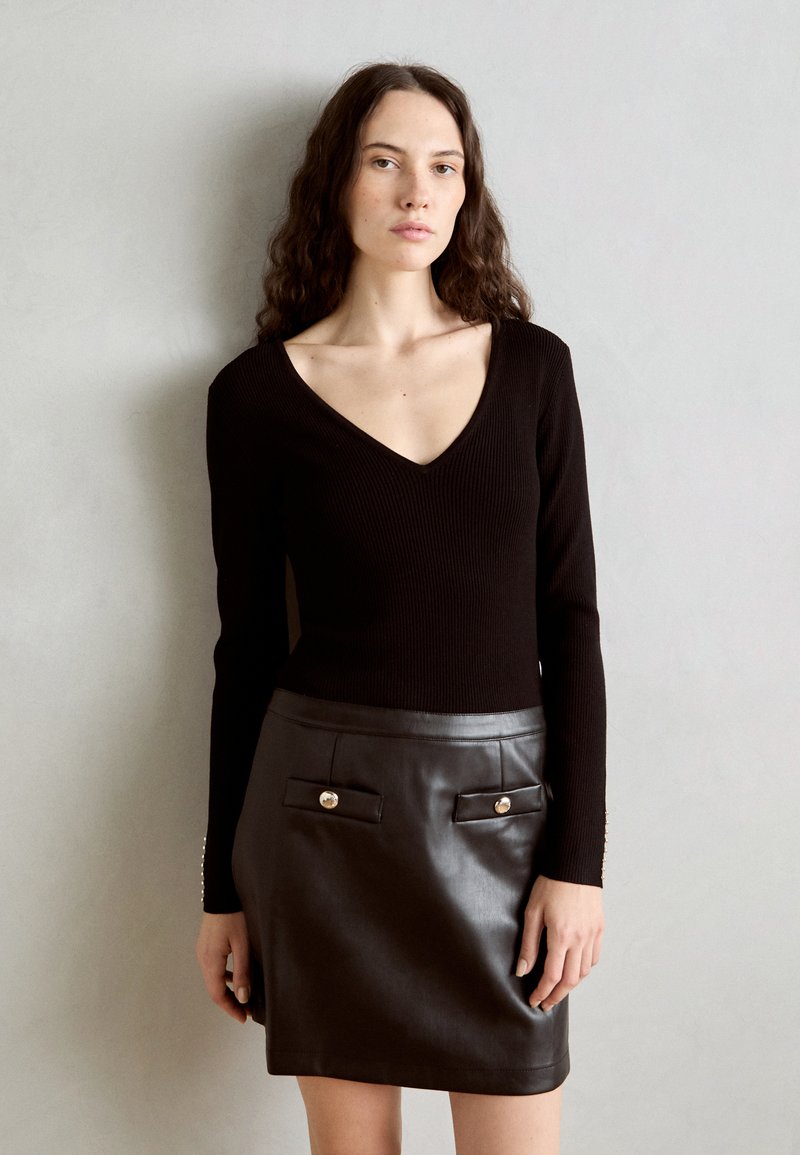 Haut en maille côtelée noire avec un col en V, associé à une mini jupe en cuir noir avec deux poches avant et des accents métalliques.