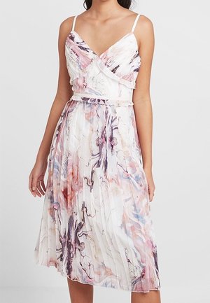Femme portant une robe midi plissée sans manches aux motifs marbrés rose, violet et bleu avec de fines bretelles.