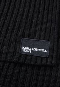 Čierna ryhovaná pletenina s obdĺžnikovou nášivkou vyšitými slovami "KARL LAGERFELD JEANS" bielou niťou.