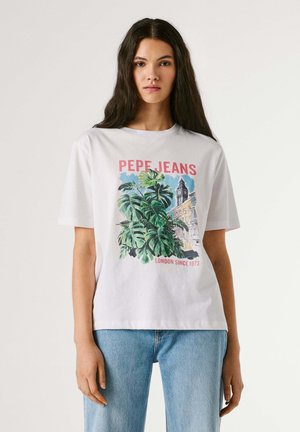 Frau mit langen dunklen Haaren, die ein weißes Pepe Jeans T-Shirt trägt, das große grüne Blätter und den Londoner Uhrenturm zeigt, kombiniert mit hellblauen Jeans.