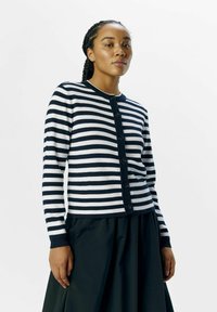 Cardigan rayé bleu marine et blanc en tricot doux, avec un col rond et des boutons sur le devant, assorti à une jupe noire.
