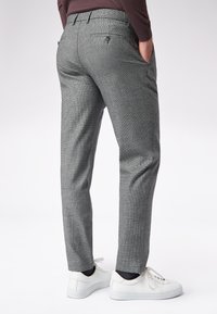 Szare w kratę spodnie charakteryzują się dopasowanym krojem, bocznymi kieszeniami i eleganckim pasem. Połączone z białymi sneakersami dla uzyskania casualowego wyglądu.