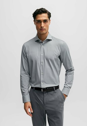 Chemise à carreaux grise à manches longues avec col et poignets à boutons. Fermeture à boutons à l'avant, associée à un pantalon gris ajusté et une ceinture noire.